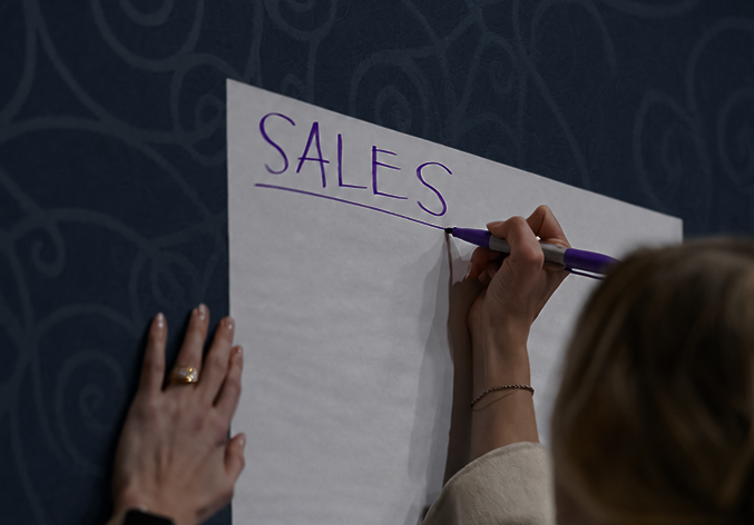 Cobalt team member writing the word "Sales" on a poster