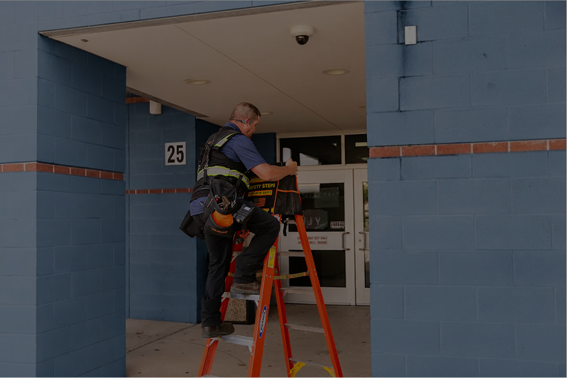 technician on ladder installing video camera outside an elementary school
