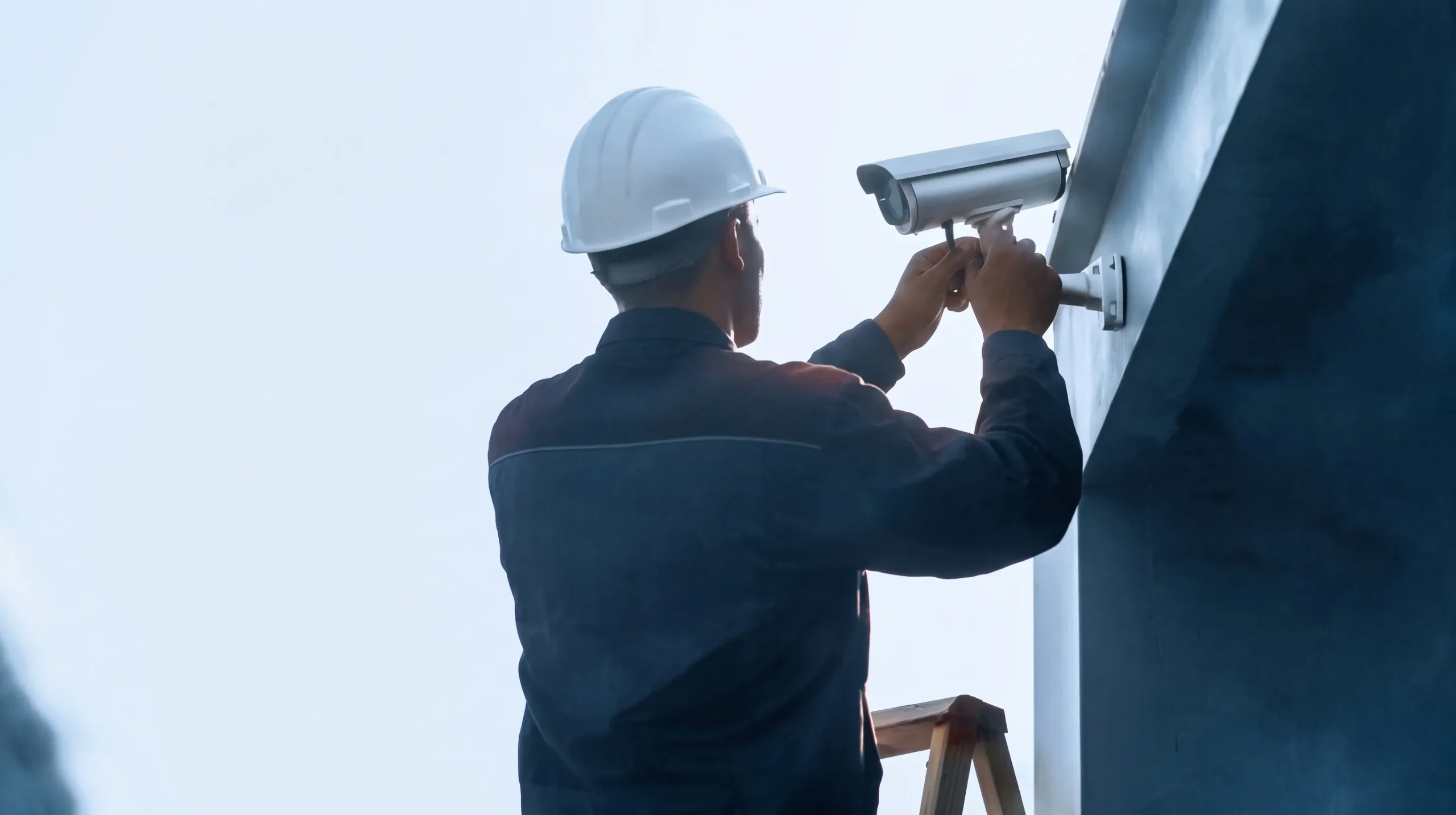 back of a worker on ladder installing surveillance camera
